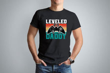 A black tshirt with a gamer remote and retro sunset design. Wording says Leveled up to Daddy on the front