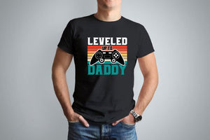 A black tshirt with a gamer remote and retro sunset design. Wording says Leveled up to Daddy on the front